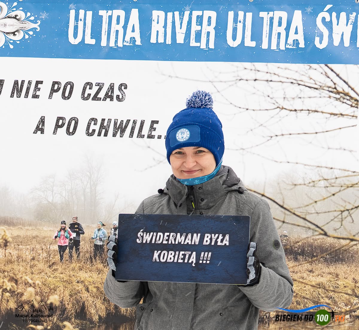 Uczestniczka URUŚ z tabliczką „Świderman była kobietą” przed banerem biegu